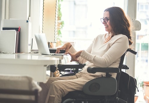 Side view of a happy woman with physical disability working on a laptop in the office.