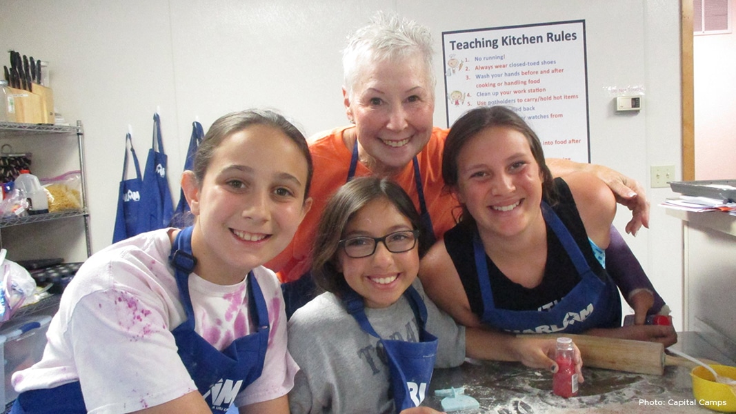 Three girls in camp kitchen, cooking with counselor