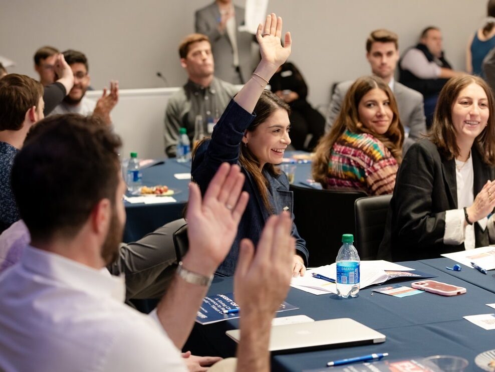 People sitting at tables, including a woman raising her hand.