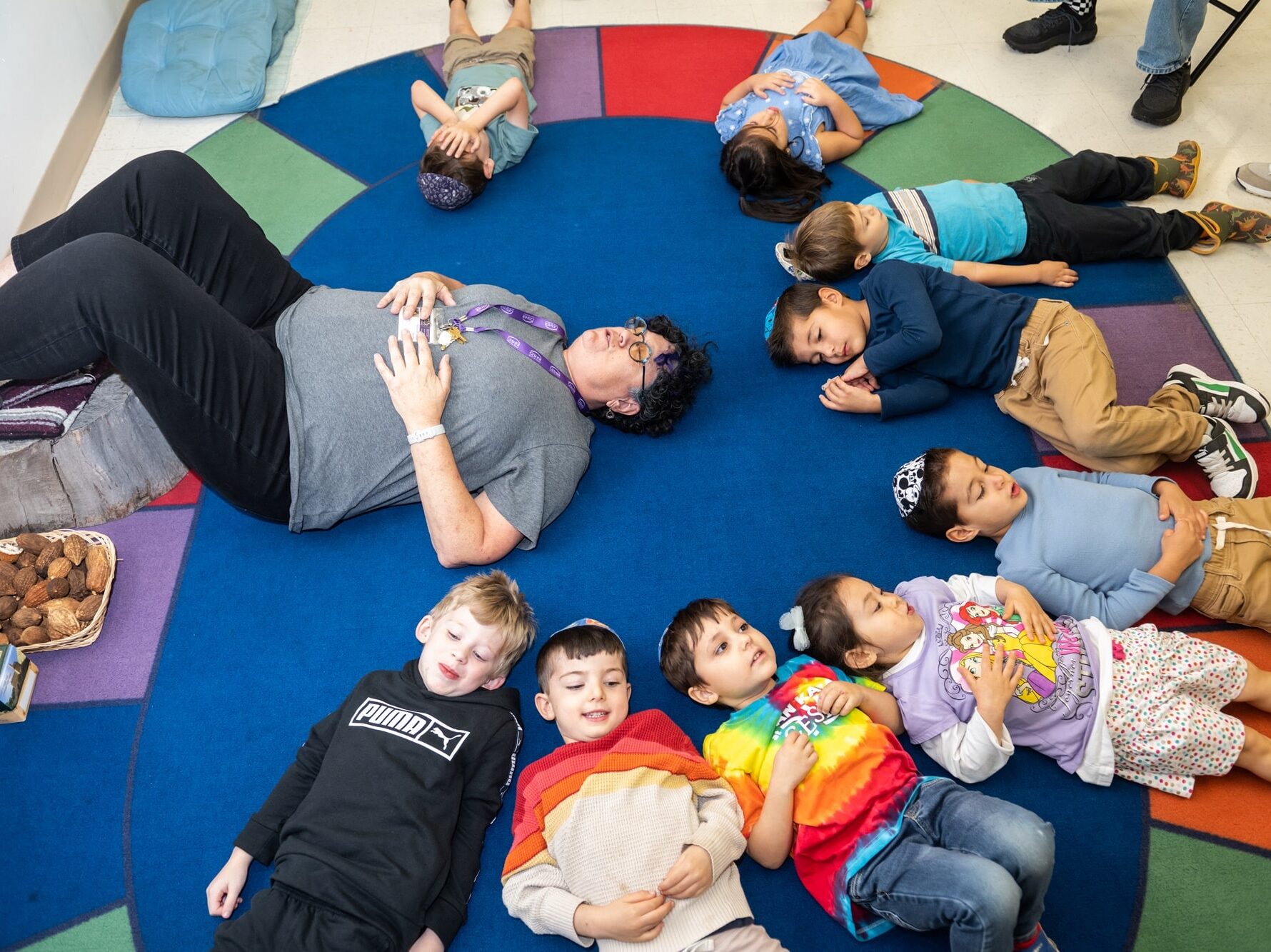 A group of children laying on a rug on the floor in a circle with teacher.