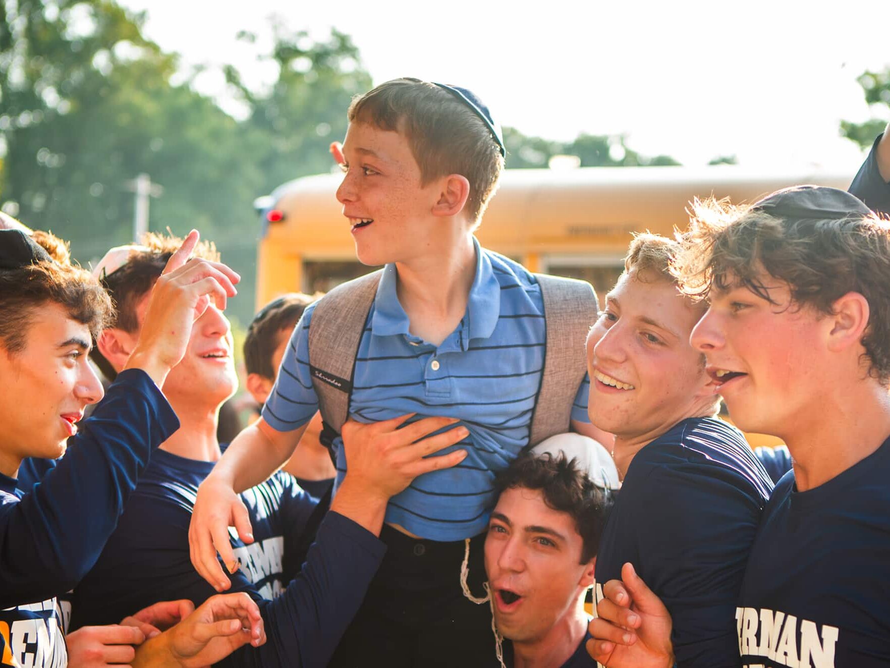 A group of smiling teens lift up a younger boy