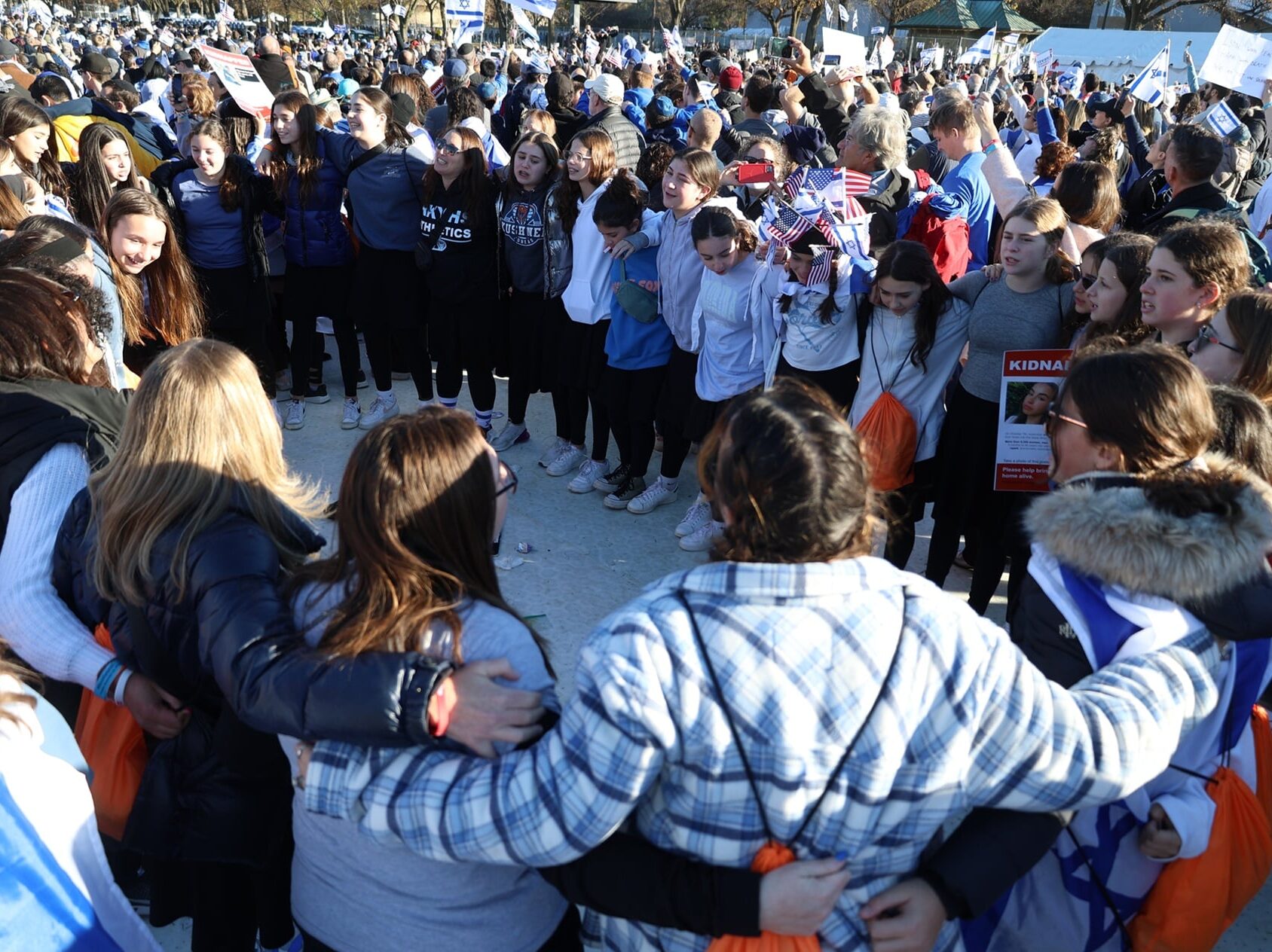 A large group stand in a circle, with arms around each other at the 2023 DC March for Israel