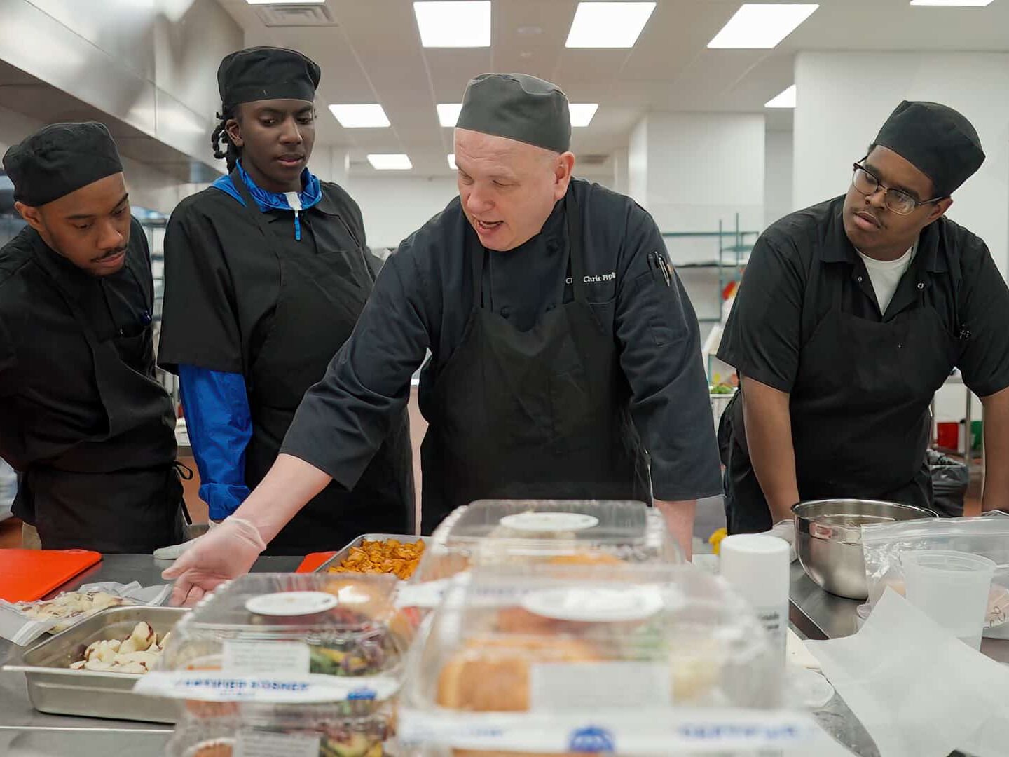 A chef teaches his three students in a kitchen