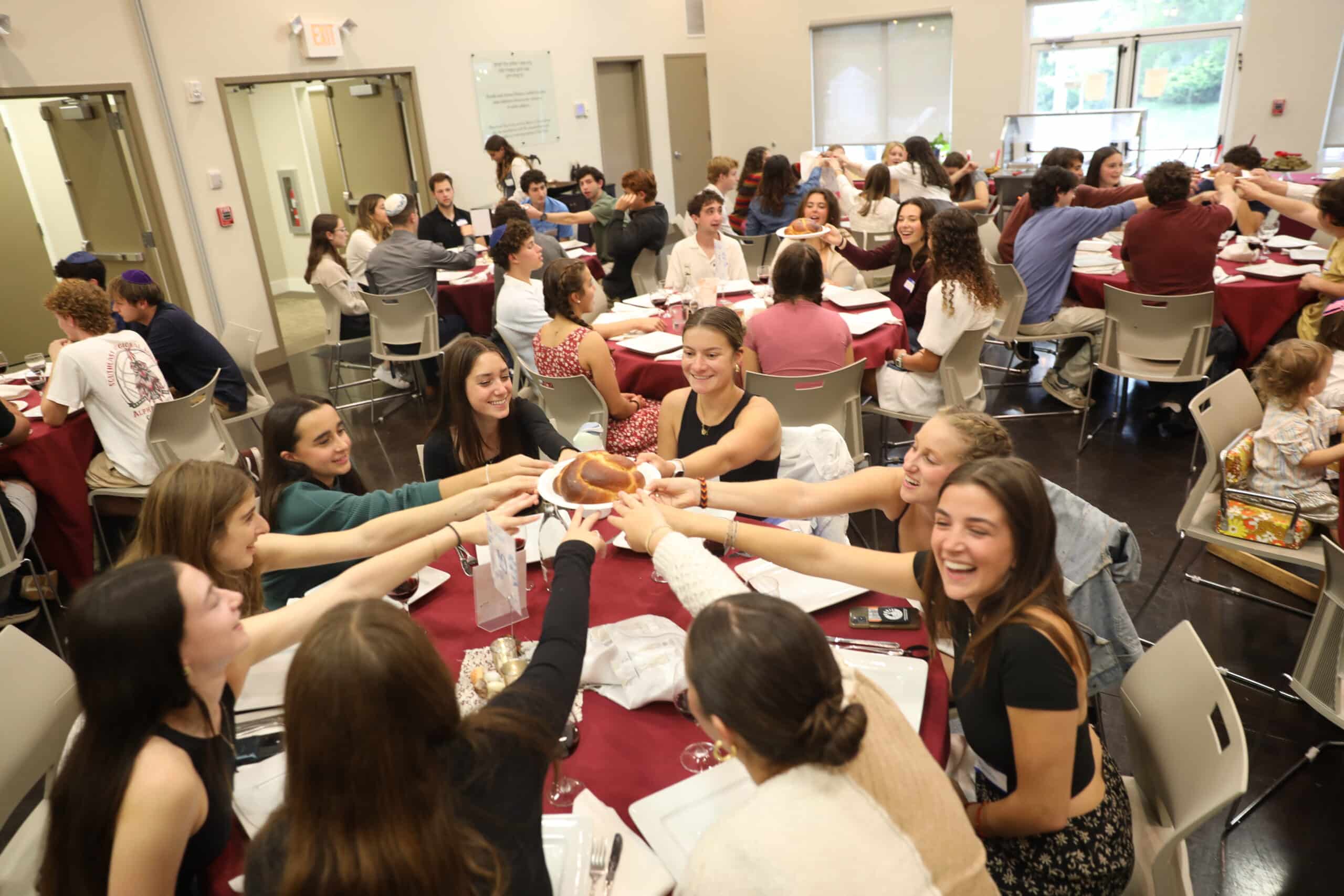 College students sitting at a table reaching toward a plate of challah.