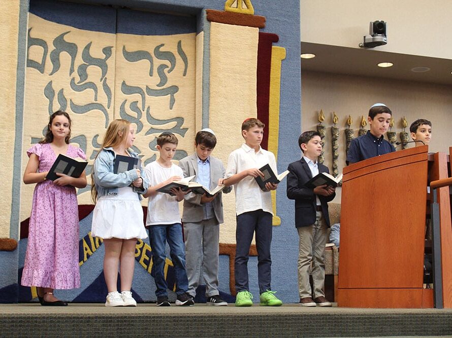 Children standing on a bimah with prayer books