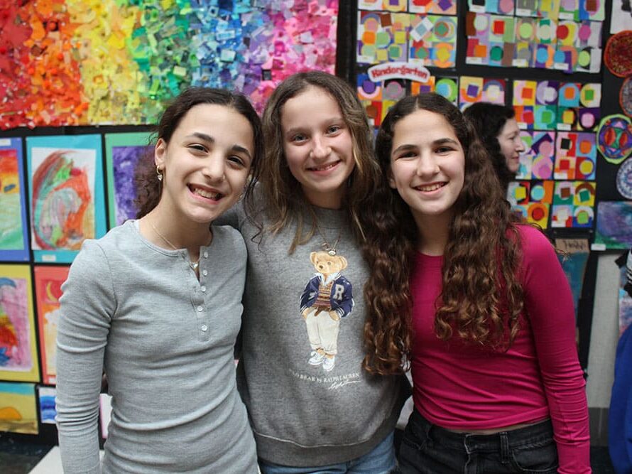 Three girls smiling together in front of a wall of artwork