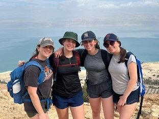 Group of teens pose on top of a mountain, with a blue sky as at the background, in the deserts of Israel.