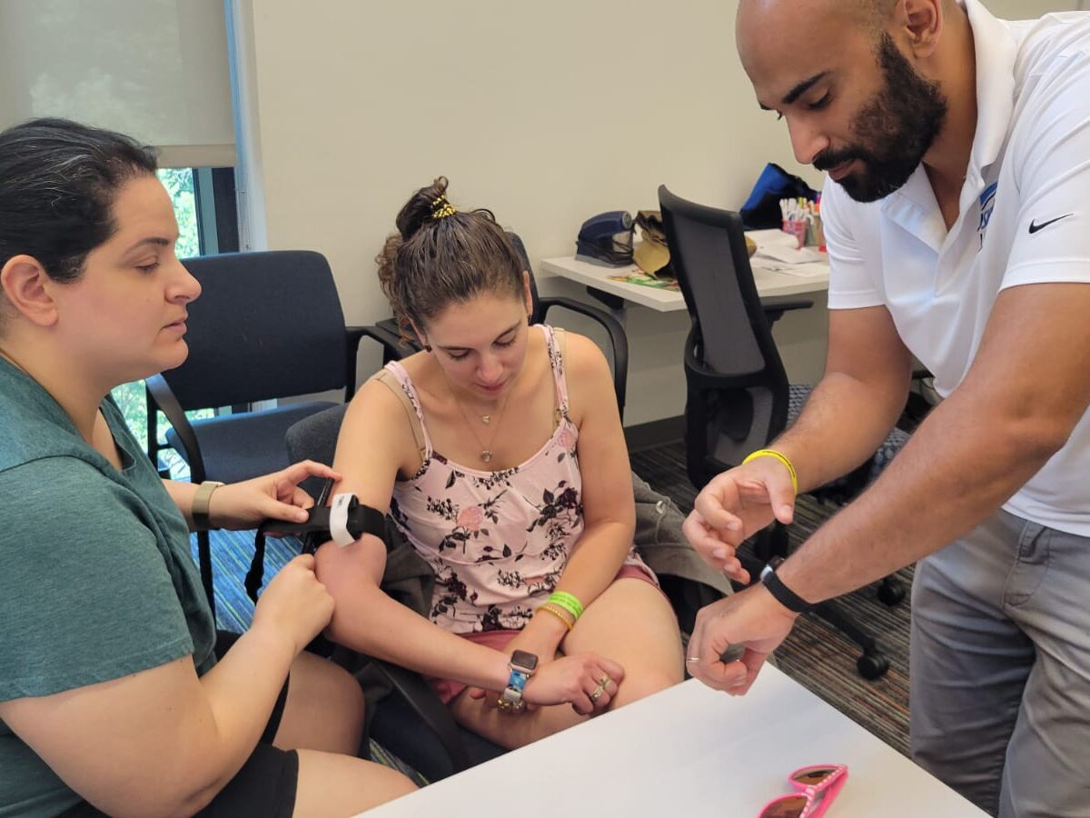 Security person demonstrating how to stop bleeding on a woman's arm, with another woman looking over.