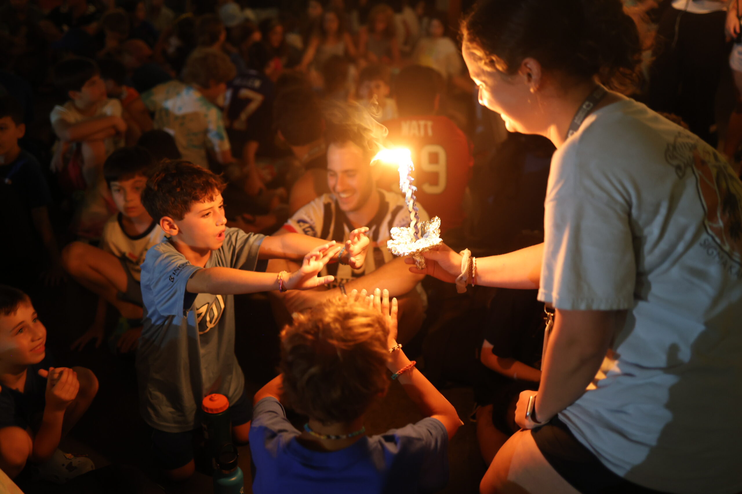 Camp children stand around a havdalah candle at night.