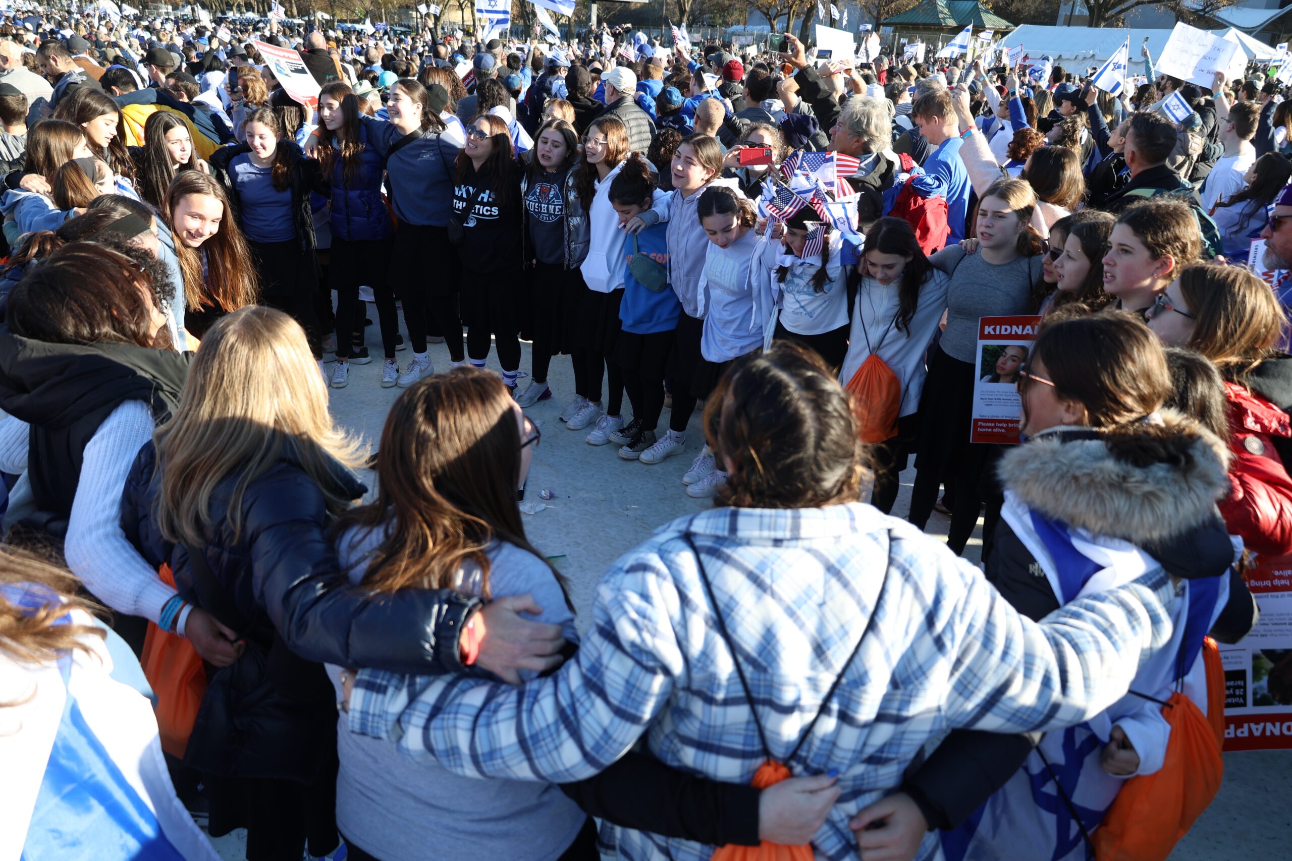 A large group stand in a circle, with arms around each other at the 2023 DC March for Israel