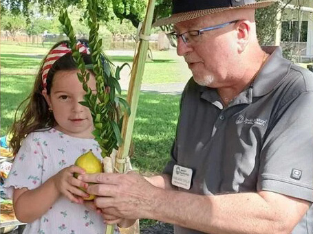 Grandfather with granddaughter holding lulav and etrog outside in sukkah